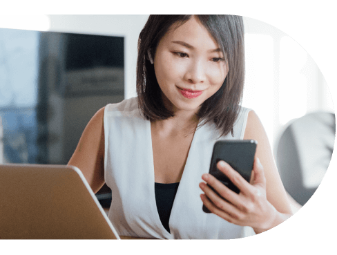 woman looking at her cellphone while working on a laptop